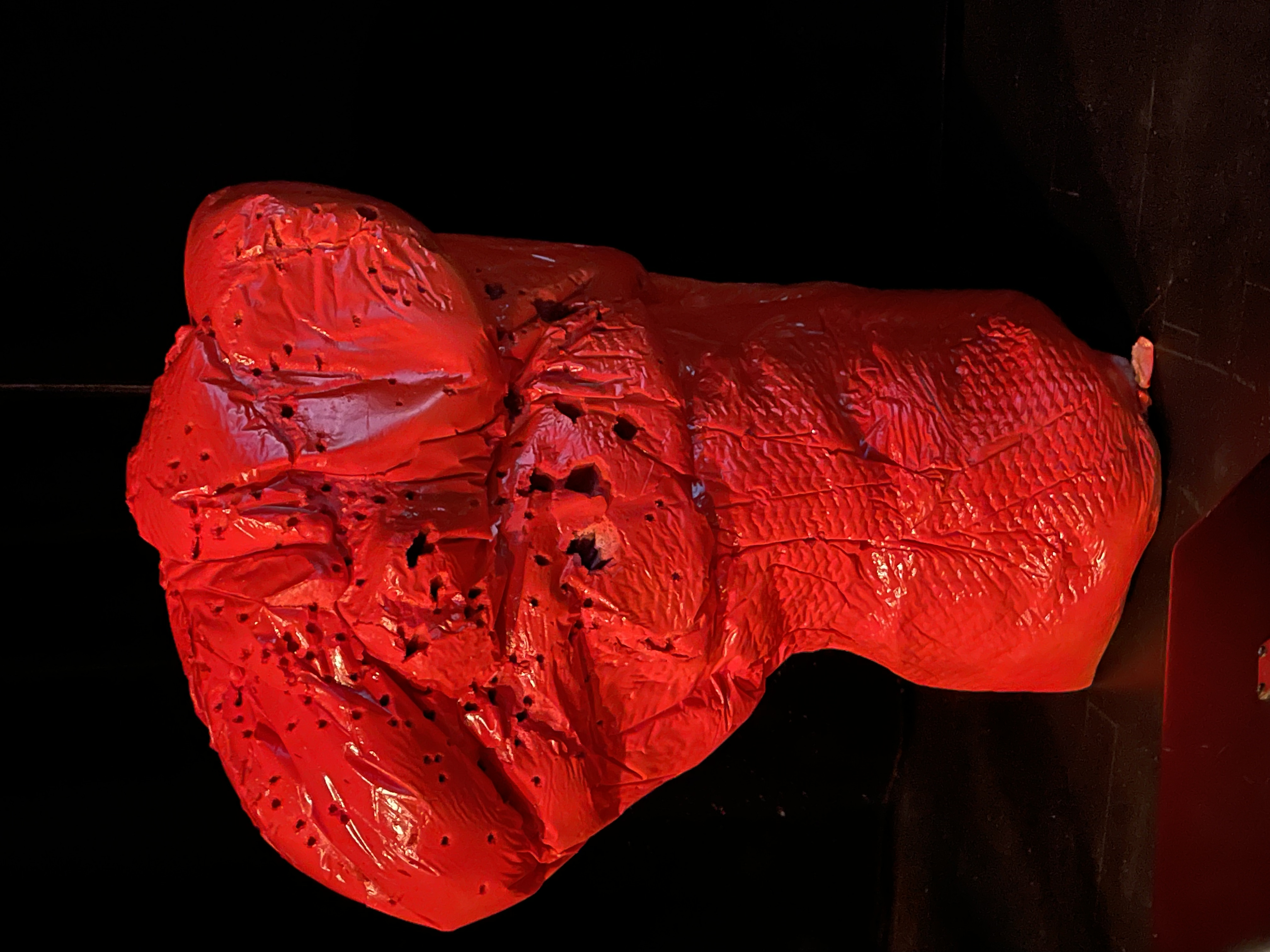 Cette phot montre la sculpture d'un buste rouge troué.